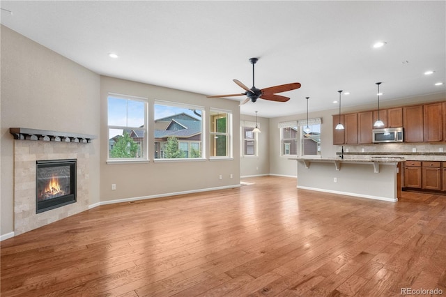 3995 Manorbrier Cir, Castle Rock, CO 80104 - unfurnished living room with light wood-type flooring, a tiled fireplace, a ceiling fan, recessed lighting, and baseboards