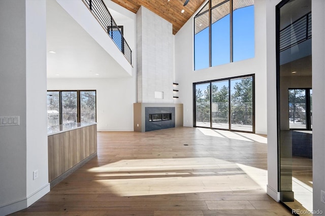 unfurnished living room featuring plenty of natural light, high vaulted ceiling, wooden ceiling, and light hardwood / wood-style flooring