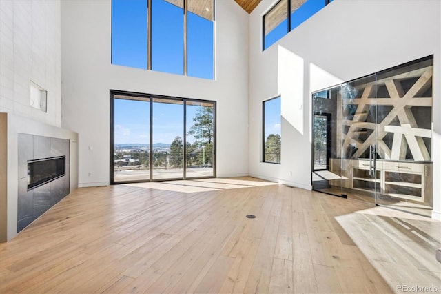 unfurnished living room with a tiled fireplace, a high ceiling, and light hardwood / wood-style flooring