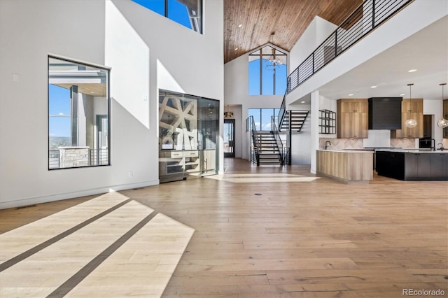 unfurnished living room featuring sink, light hardwood / wood-style flooring, a towering ceiling, and a notable chandelier