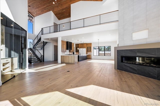 unfurnished living room featuring a fireplace, light hardwood / wood-style flooring, a towering ceiling, and wood ceiling