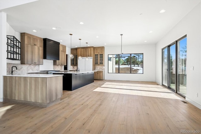 kitchen with light wood-type flooring, tasteful backsplash, a kitchen island, and hanging light fixtures