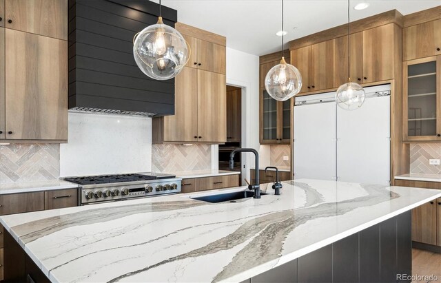 kitchen with sink, decorative backsplash, light stone countertops, range hood, and decorative light fixtures