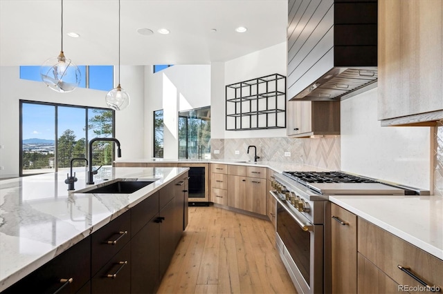 kitchen with premium range hood, sink, light hardwood / wood-style flooring, stainless steel range, and decorative light fixtures