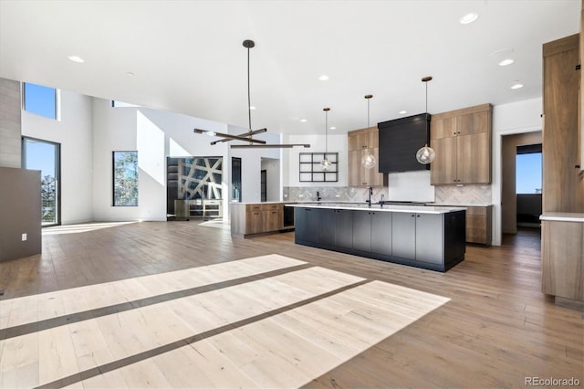 kitchen featuring sink, backsplash, a large island with sink, pendant lighting, and light hardwood / wood-style floors