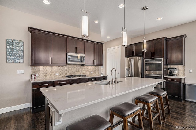 kitchen featuring sink, stainless steel appliances, hanging light fixtures, and a center island with sink