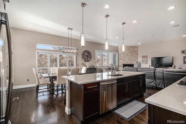 kitchen featuring an island with sink, dishwasher, sink, and hanging light fixtures