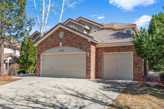 traditional-style house with an attached garage, stucco siding, concrete driveway, a tiled roof, and brick siding