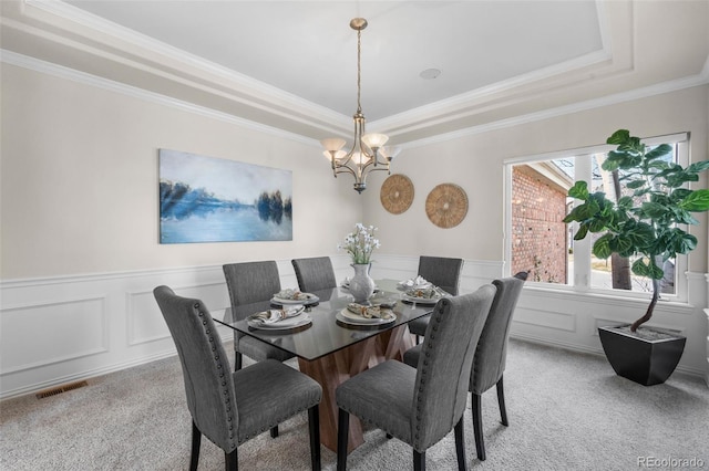 dining area with a wainscoted wall, visible vents, light carpet, a raised ceiling, and a chandelier