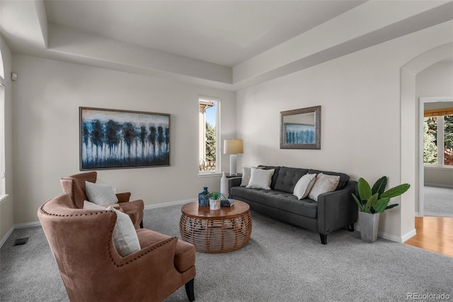 living area with a raised ceiling, arched walkways, visible vents, and baseboards