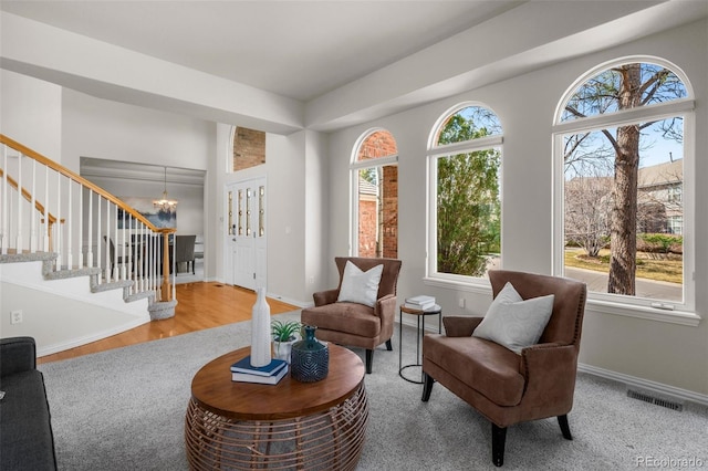 living area with visible vents, wood finished floors, stairway, an inviting chandelier, and baseboards