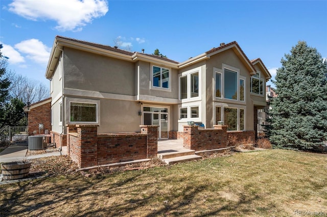 rear view of house featuring stucco siding, brick siding, central AC, and a lawn