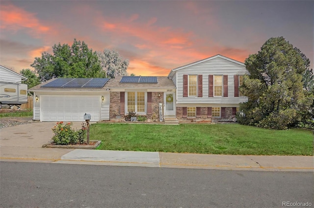 18527 E Kansas Pl, Aurora, CO 80017 - tri-level home with an attached garage, driveway, a yard, roof mounted solar panels, and brick siding