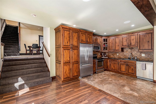 kitchen featuring dark countertops, a sink, decorative backsplash, appliances with stainless steel finishes, and dark wood-style flooring