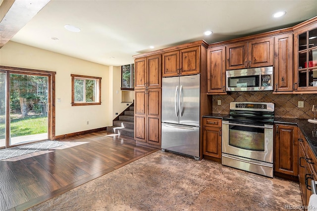 kitchen with dark wood finished floors, decorative backsplash, appliances with stainless steel finishes, and glass insert cabinets