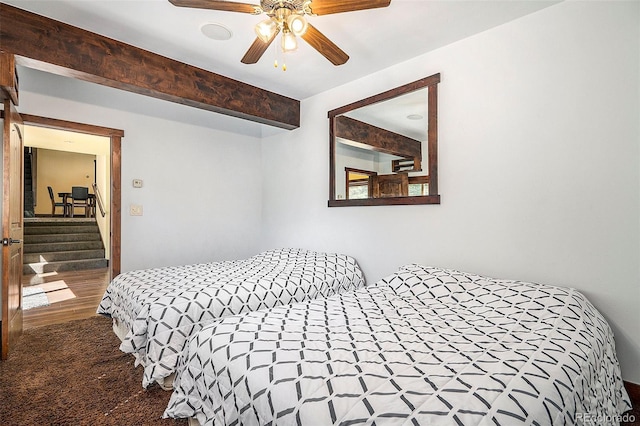 carpeted bedroom with beam ceiling and a ceiling fan