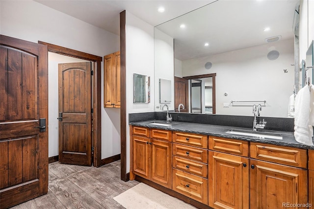 full bathroom featuring a sink, baseboards, wood finished floors, and double vanity