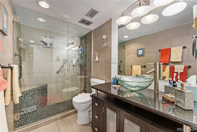 bathroom featuring a shower with door, toilet, vanity, tile walls, and tile patterned floors