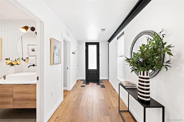 foyer featuring light wood finished floors, visible vents, wallpapered walls, and baseboards