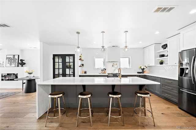 kitchen featuring open shelves, visible vents, stainless steel fridge, and light wood finished floors