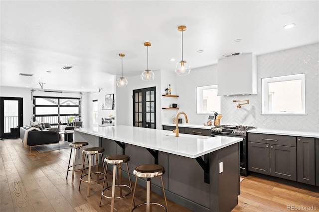 kitchen with tasteful backsplash, light wood-type flooring, light countertops, stainless steel gas stove, and a sink