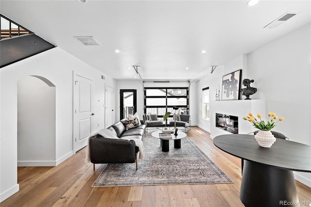 living area with light wood finished floors, arched walkways, visible vents, and a multi sided fireplace