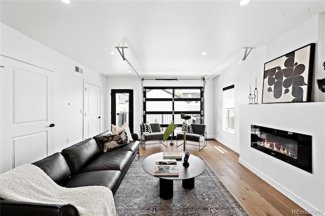 living room featuring visible vents, a glass covered fireplace, recessed lighting, light wood finished floors, and baseboards