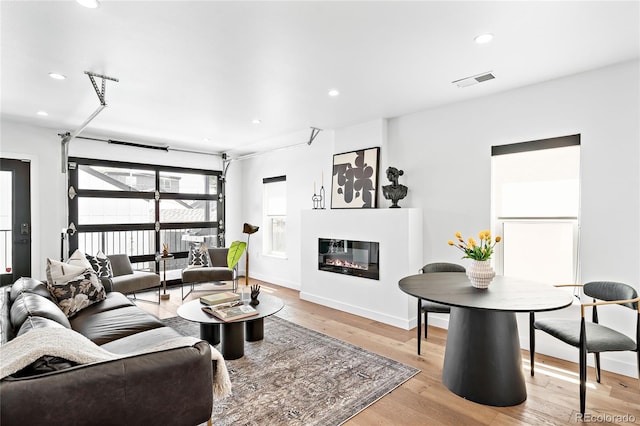 living area featuring visible vents, light wood finished floors, baseboards, recessed lighting, and a glass covered fireplace