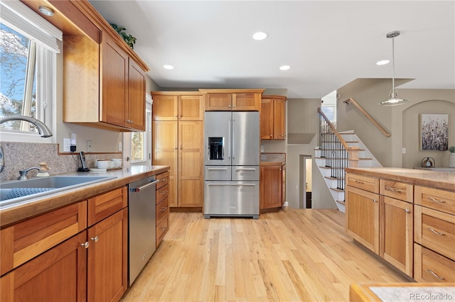 kitchen with light wood finished floors, a sink, light countertops, appliances with stainless steel finishes, and pendant lighting