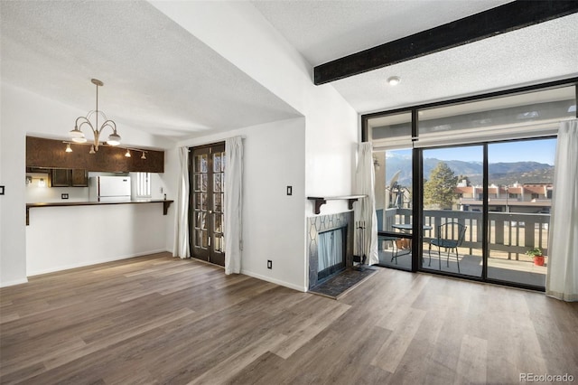 unfurnished living room featuring a mountain view, vaulted ceiling with beams, a textured ceiling, wood-type flooring, and a chandelier