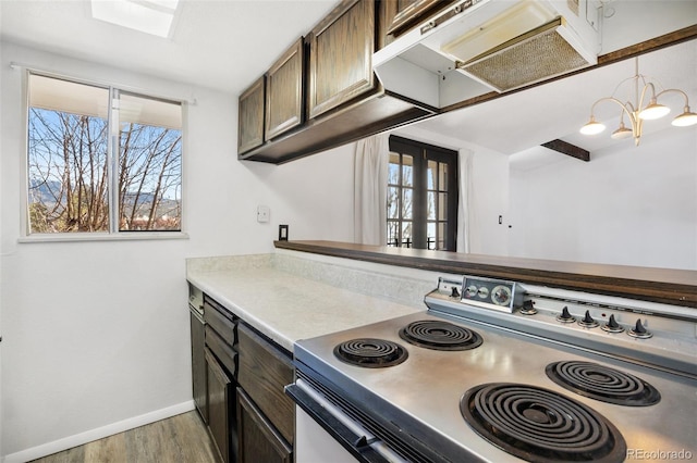 kitchen with dark brown cabinetry, range with electric cooktop, a skylight, a notable chandelier, and hardwood / wood-style floors