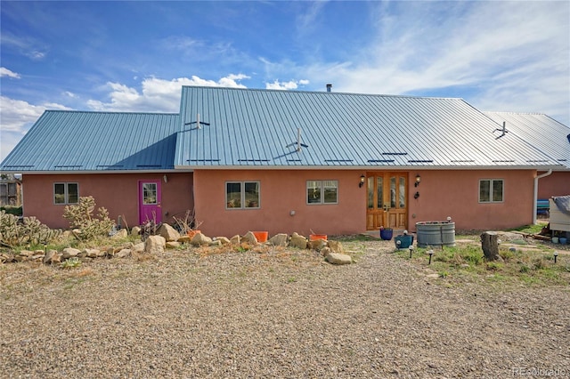 rear view of house featuring a standing seam roof, stucco siding, and metal roof