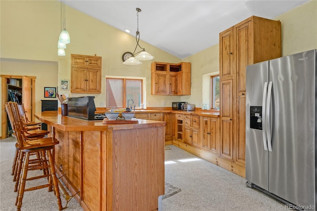 kitchen with a breakfast bar, light carpet, high vaulted ceiling, stainless steel fridge with ice dispenser, and hanging light fixtures