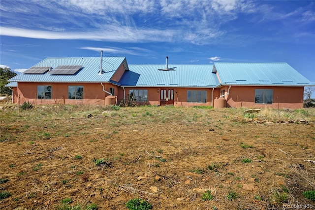 view of front of house with roof mounted solar panels, stucco siding, and metal roof