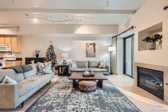 living room with beamed ceiling, light hardwood / wood-style floors, and a tile fireplace