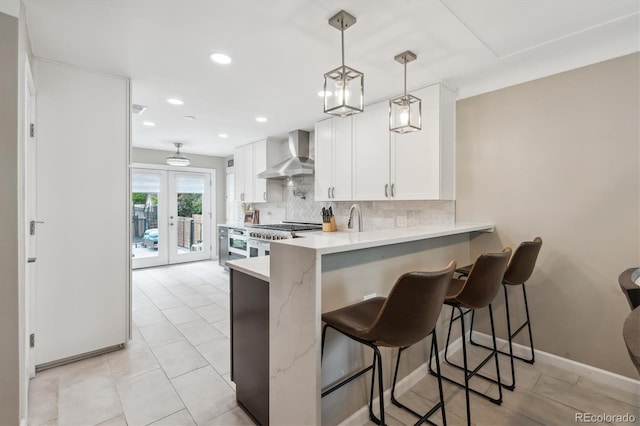 2664 Forest St, Denver, CO 80207 - kitchen with wall chimney range hood, decorative backsplash, white cabinetry, recessed lighting, and a breakfast bar