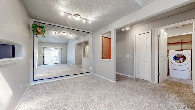 carpeted empty room with track lighting, a textured ceiling, washer / clothes dryer, and baseboards