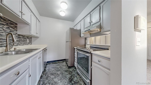 kitchen featuring tasteful backsplash, under cabinet range hood, light countertops, appliances with stainless steel finishes, and a sink