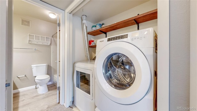 clothes washing area with washer and dryer, baseboards, visible vents, and light wood-type flooring