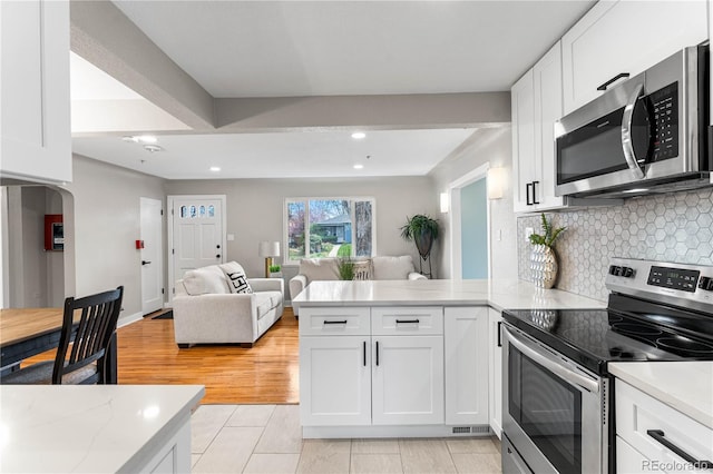 kitchen featuring a peninsula, arched walkways, white cabinets, appliances with stainless steel finishes, and open floor plan