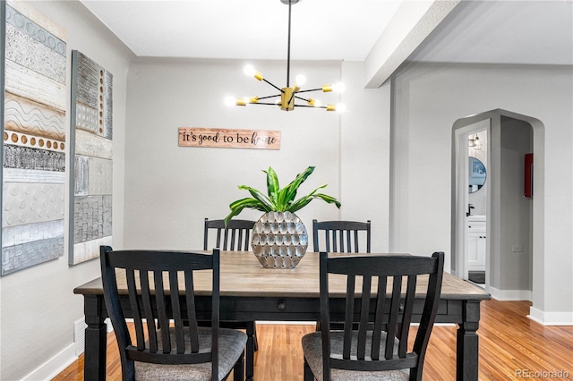 dining area featuring baseboards, arched walkways, an inviting chandelier, and wood finished floors