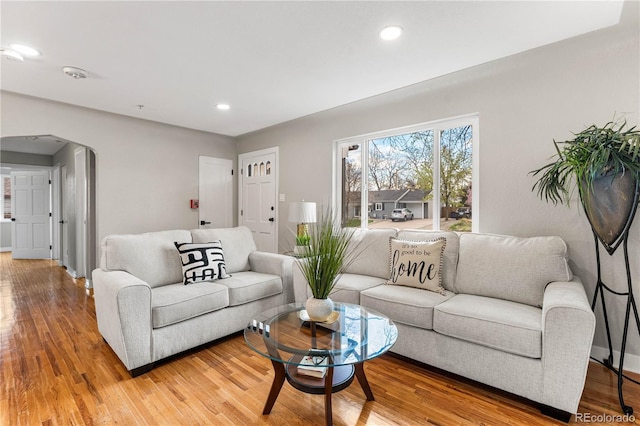 living area featuring recessed lighting, baseboards, arched walkways, and light wood-style flooring