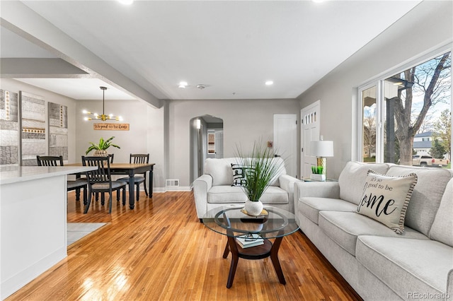 living room with baseboards, beam ceiling, arched walkways, light wood-style floors, and a notable chandelier