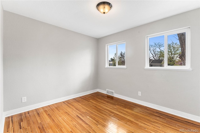 empty room with hardwood / wood-style flooring, baseboards, and visible vents