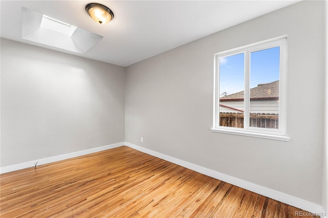 unfurnished room featuring a skylight, light wood-style flooring, and baseboards