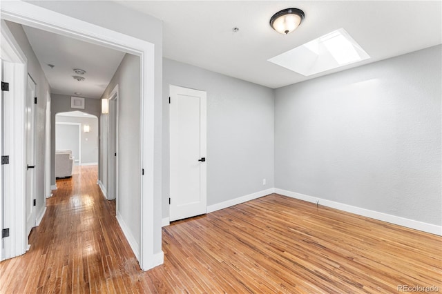 hall with arched walkways, a skylight, baseboards, and wood finished floors