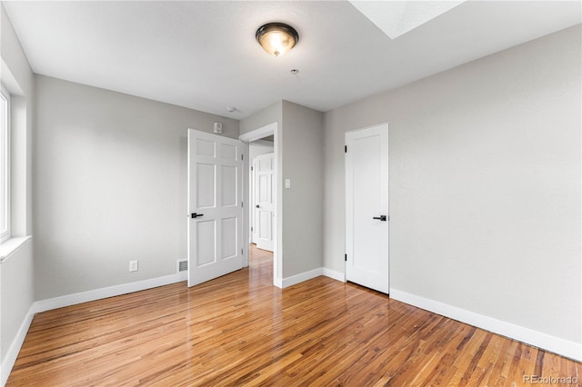 unfurnished bedroom with light wood-type flooring, baseboards, multiple windows, and a skylight