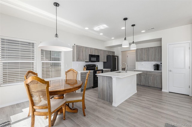 kitchen with a center island with sink, black appliances, light hardwood / wood-style flooring, and decorative light fixtures