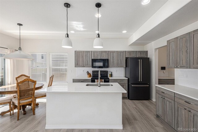 kitchen with a kitchen island with sink, light hardwood / wood-style flooring, black appliances, sink, and decorative light fixtures