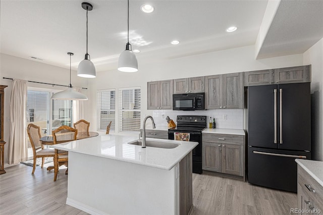 kitchen with black appliances, sink, an island with sink, and hanging light fixtures